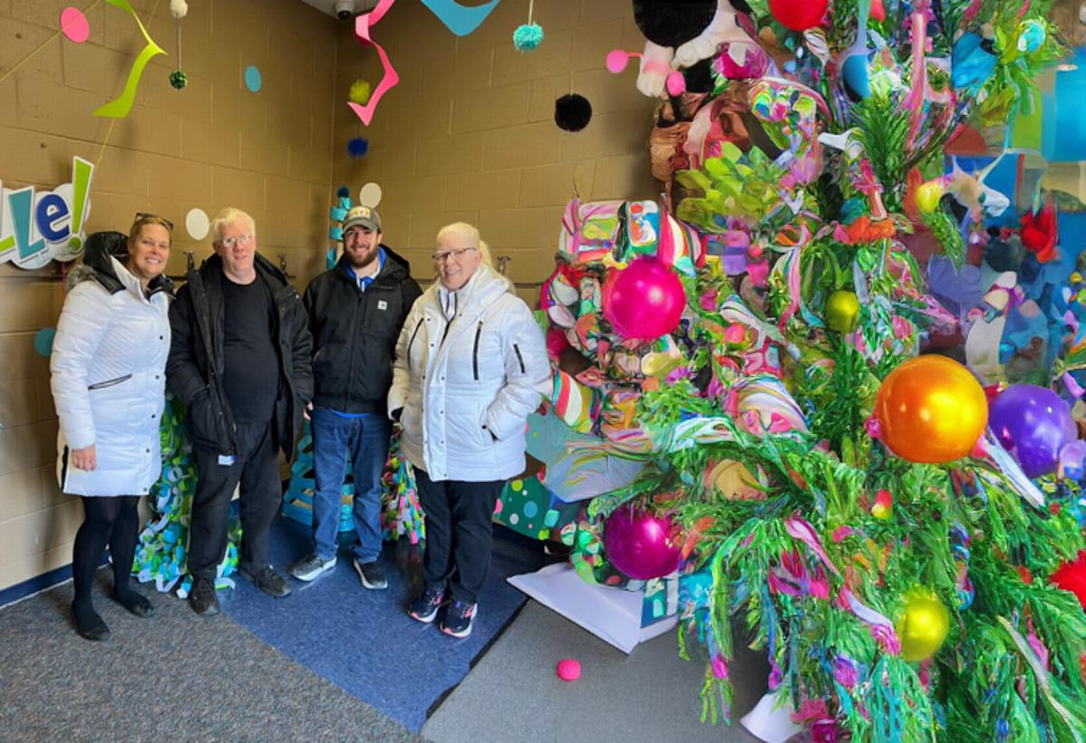 Four people in a picture with a Christmas tree to the right.