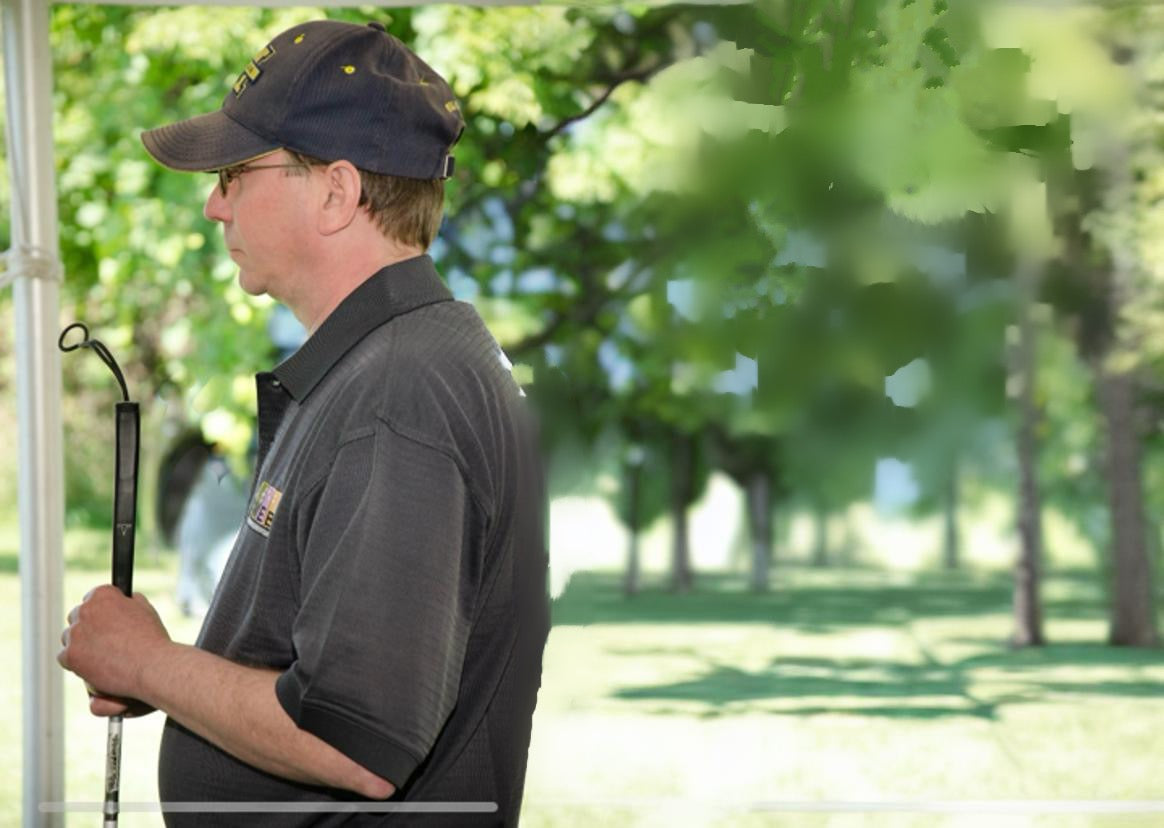 A picture of a man holding a cane. Trees are behind him.